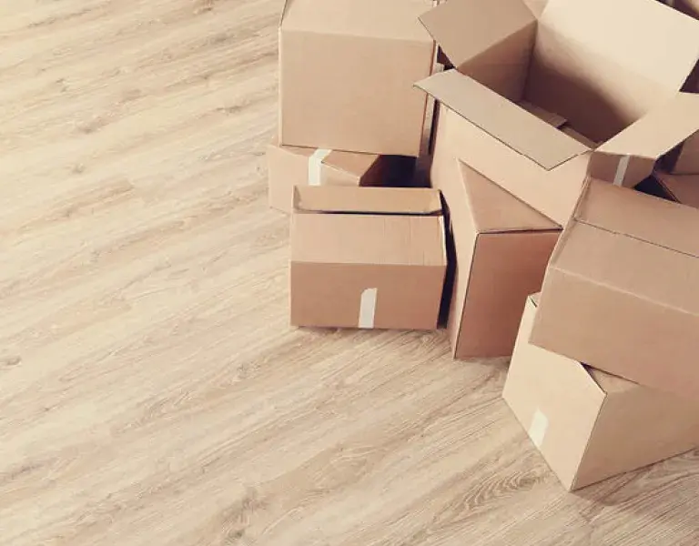 Mehrere braune Pappkartons, teils offen, stehen auf einem hellen Holzfußboden und dienen zum Transport oder Einräumen von Küchen- und Möbelteilen.